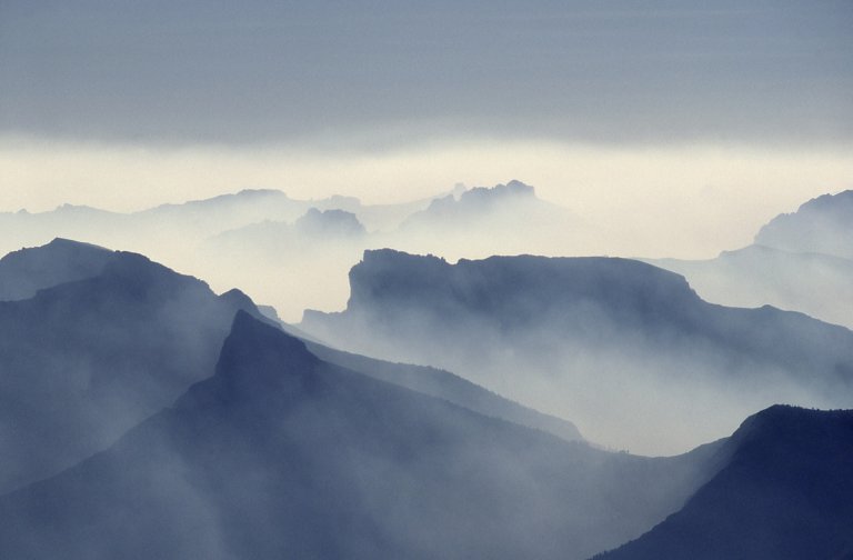 A misty mountain range with jagged peaks shrouded in fog and clouds