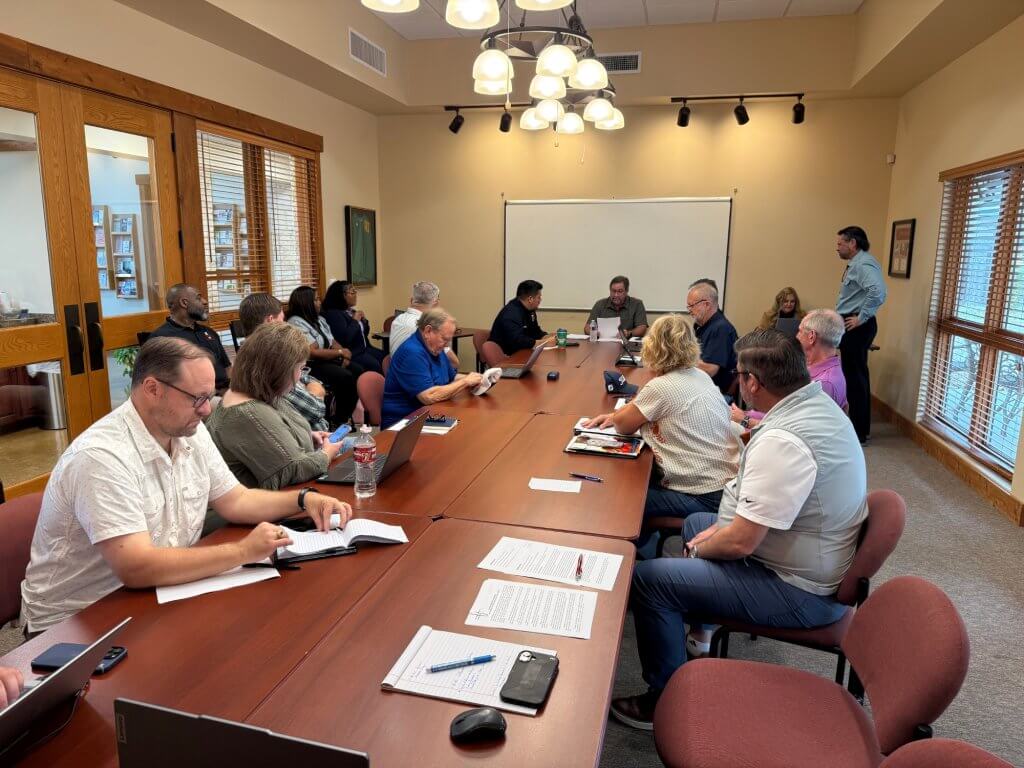 A group of people are gathered around a long table in a conference room, engaged in a meeting