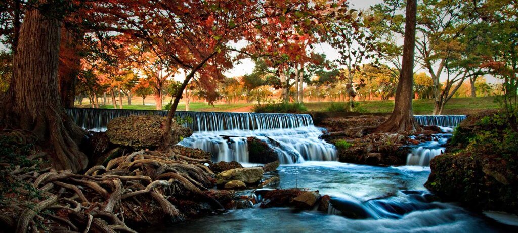 A serene autumn waterfall cascades through a colorful forest with vibrant red and orange leaves