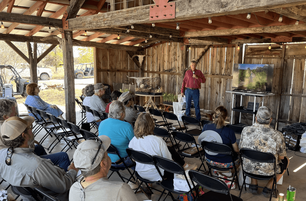 People gather in a rustic wooden barn to watch a presentation on a large screen