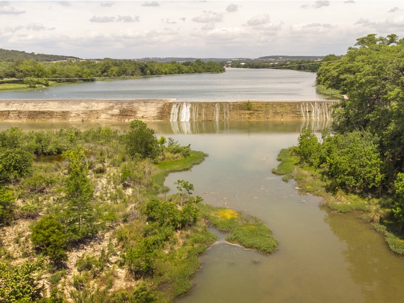 Aerial view of a river with a waterfall, surrounded by lush greenery and trees