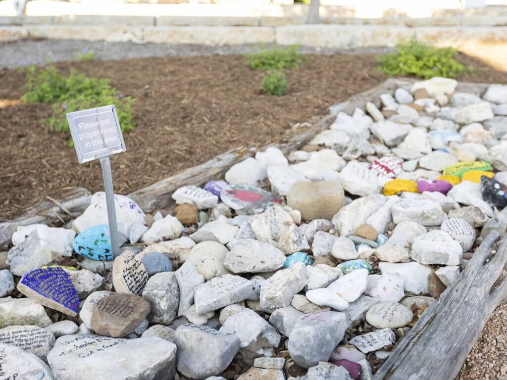 A winding stone path with colorful painted rocks and a sign inviting prayer